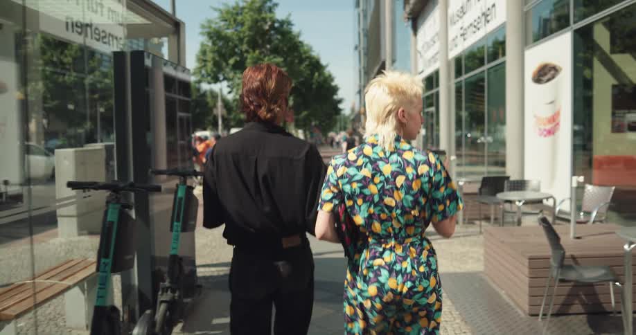 Two people are walking down a city street looking at the shops