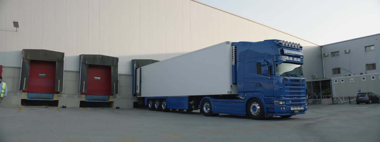 A large blue semi truck being unloaded into a warehouse