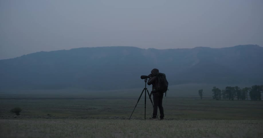 Professional photographer wearing a backpack taking pictures of landscape in nature with his professional camera on a tripod