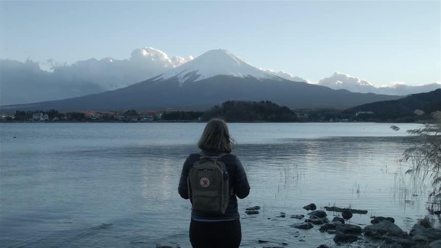 A woman wearing a backpack looks over a lake