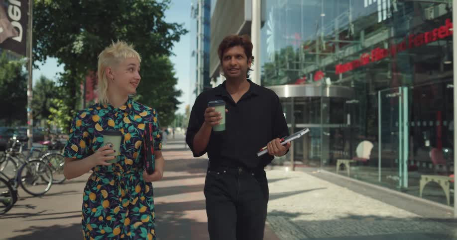 Two people walking down a city sidewalk sipping coffee and talking