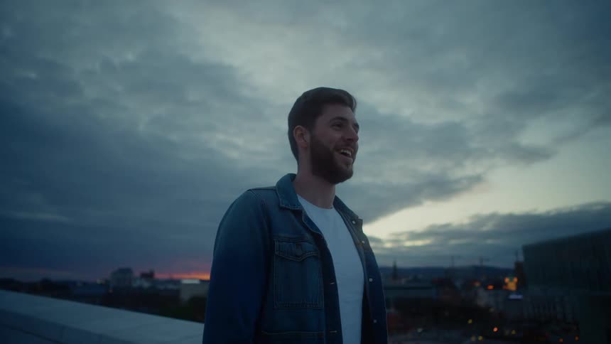 Man stands on roof looking around city under a red tinted horizon