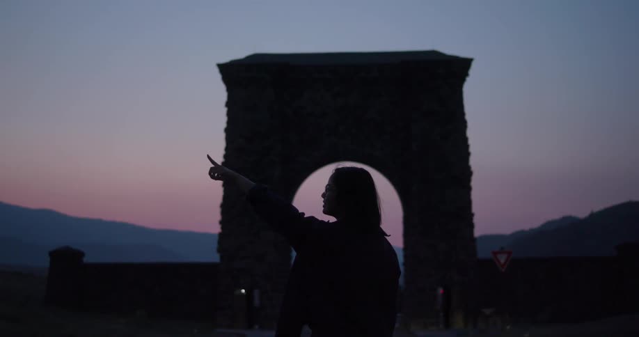 A woman is standing outdoors while the sun is setting
