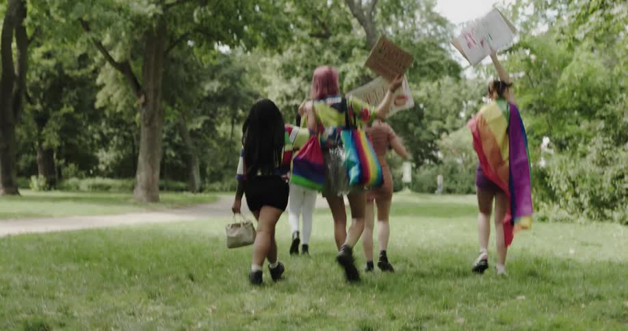 A group of lgbtq friends walk together carrying signs and wearing rainbows