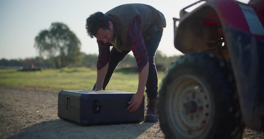A man lays a large carrying case on a dirt road and begins to unpack the drone within