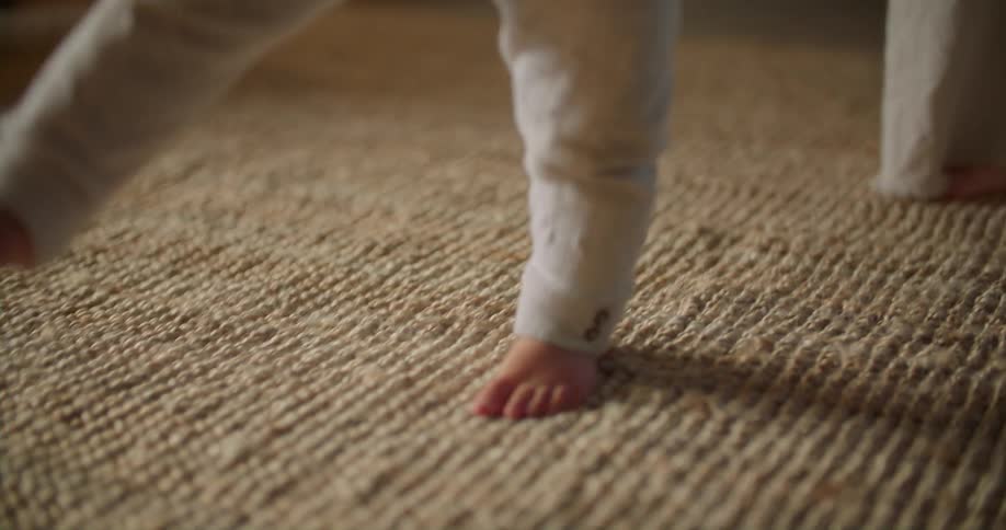 Mother follows closely as child toddlers across carpet