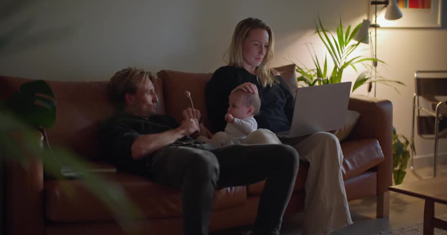 Parents spend time with baby on sofa as mother works on laptop