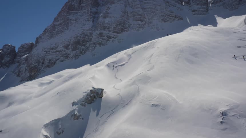 A skier standing high in the mountains begins to ski down a wide slope