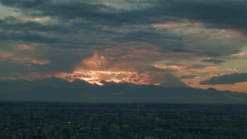The sun sets behind clouds over a city