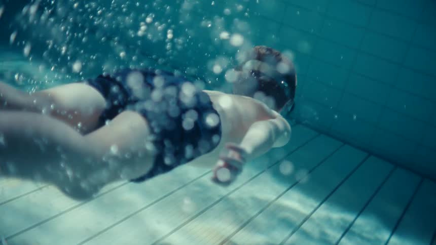A young boy swims under water in a pool