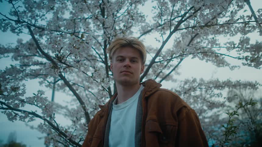 A man looks into the camera while standing before a blossoming tree in the evening