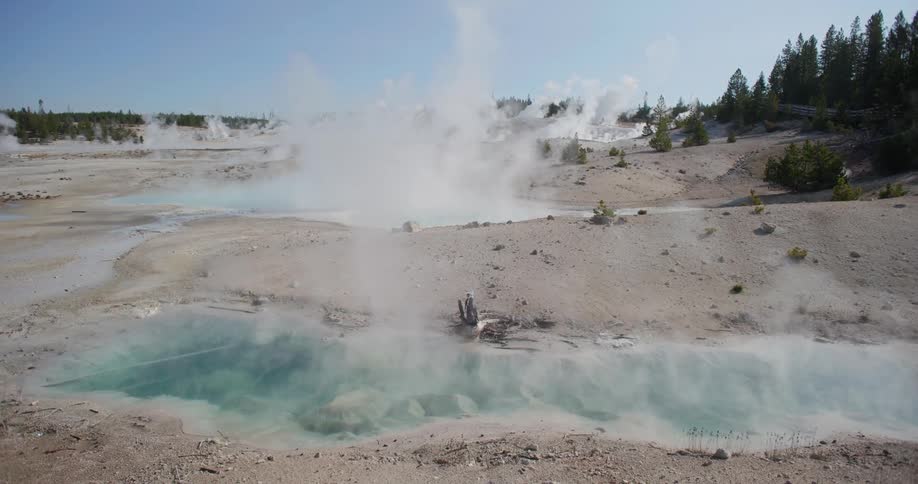 Steam is rising from the hot springs of a national park during the daytime
