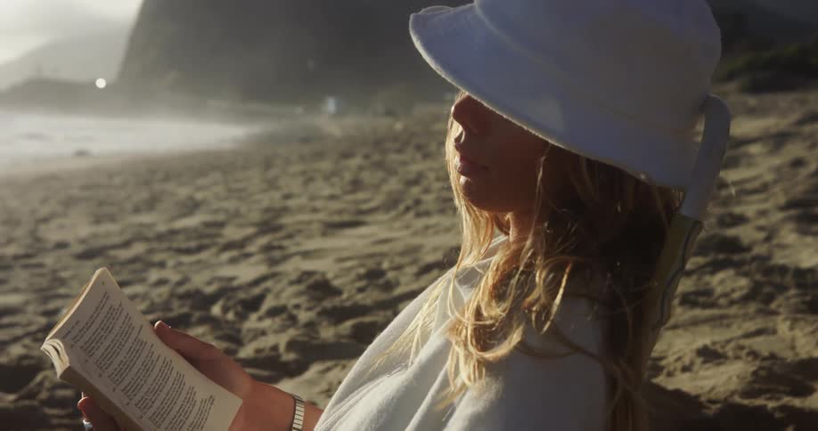 A woman is sitting at the beach and reading a book