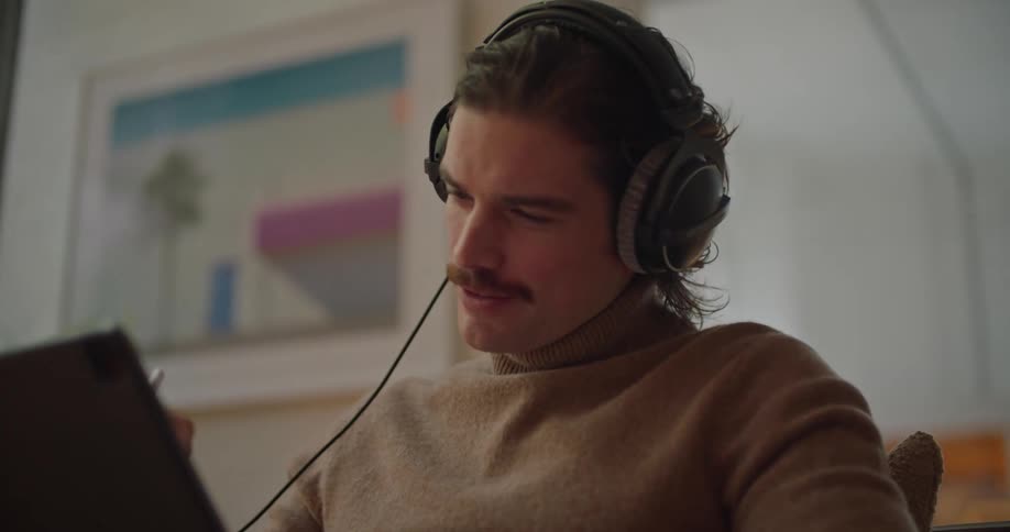 Man wearing headphones listening to a podcast and taking notes