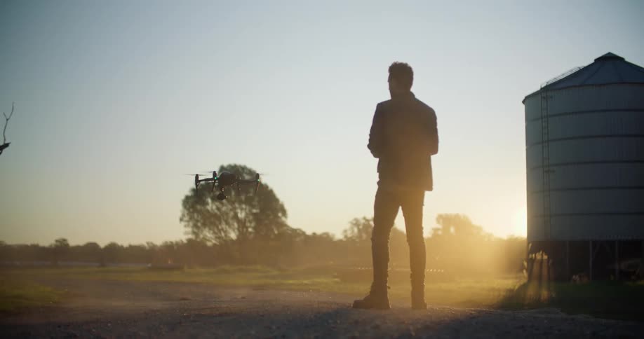 A man flying a drone in a rural area at sunset