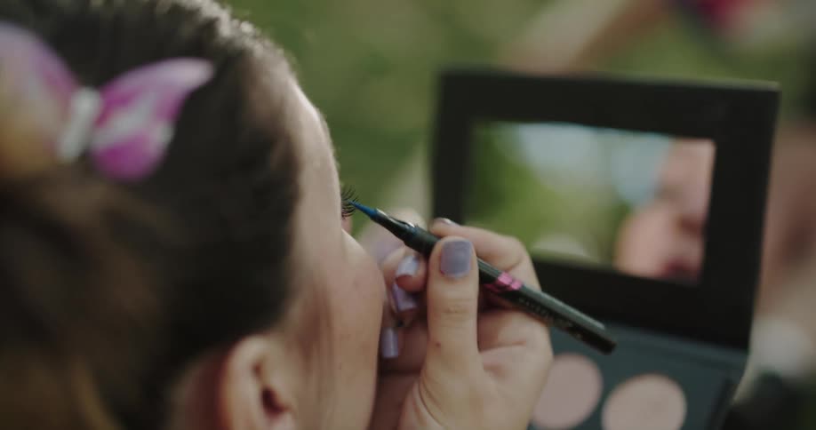 A woman is sitting outdoors and doing her makeup