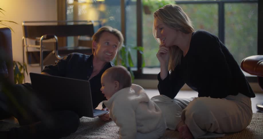 Family sitting on carpet in living room watching on a laptop