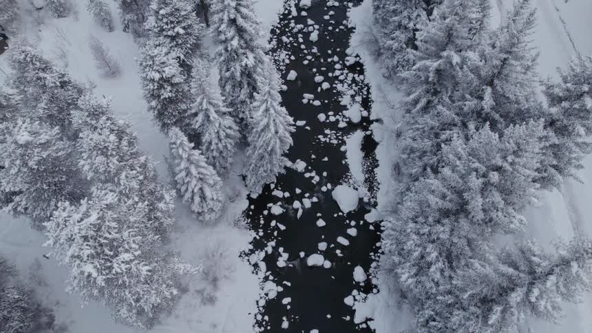 Aerial of a river with ice chunks along a forest covered in snow