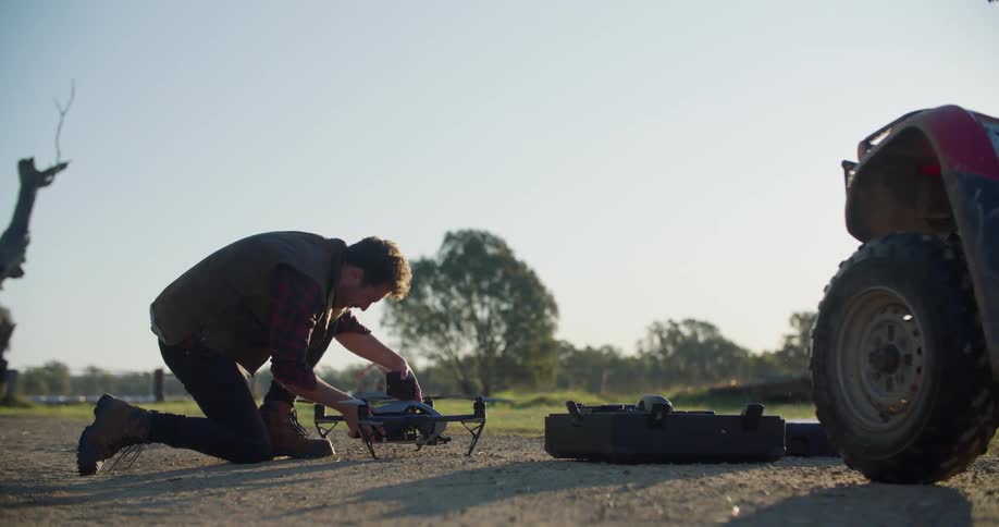 A man retrieves a part from a case and kneels to attach the part to a drone resting on the ground