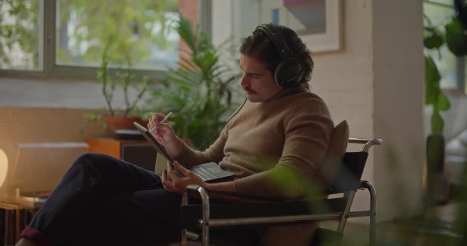 A man sits in an office and contemplates what to write on his tablet then writes it