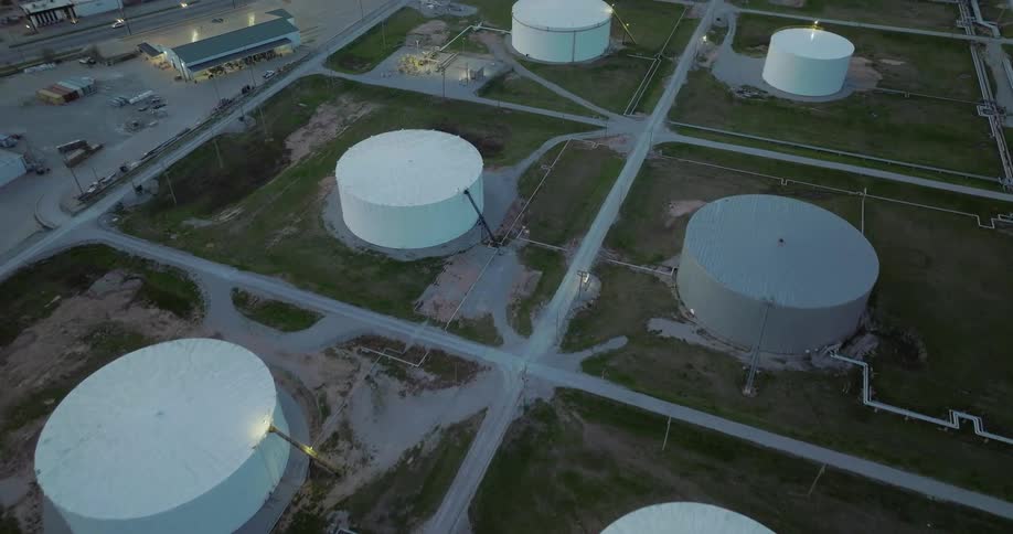 A series of large storage tanks in a refinery in the evening