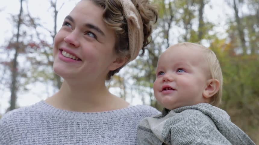 A smiling woman holds a baby outside during the day