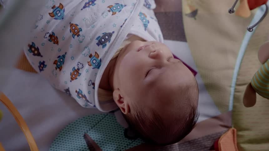 A baby sleeps in a cradle while wrapped in a small blanket