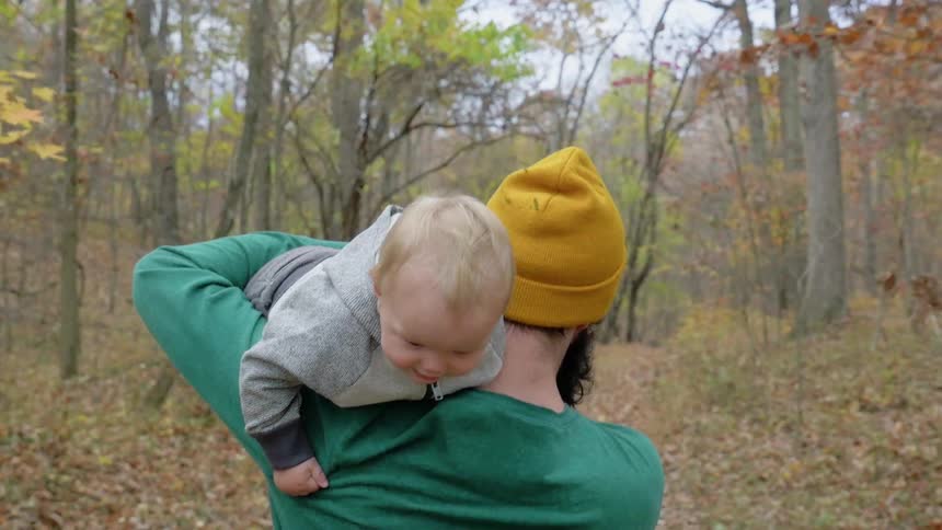 A man puts a baby on his shoulder and walks into the forest