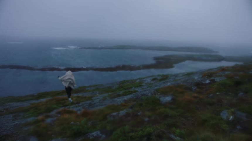 A person descends a rocky slope on a windy coast under a cloudy daytime sky