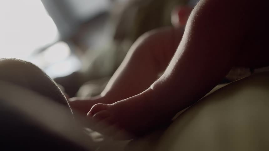 A baby moves it legs while lying on a bed indoors during the day