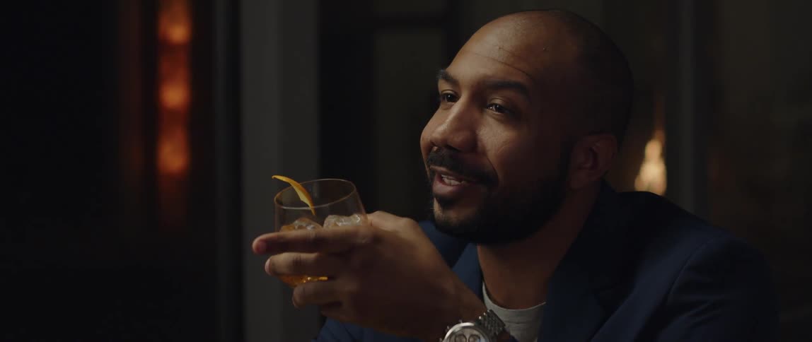 Middle aged man drinking a whiskey and holding a conversation at a bar during the night