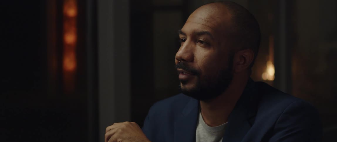 A man is sitting indoors and talking to someone
