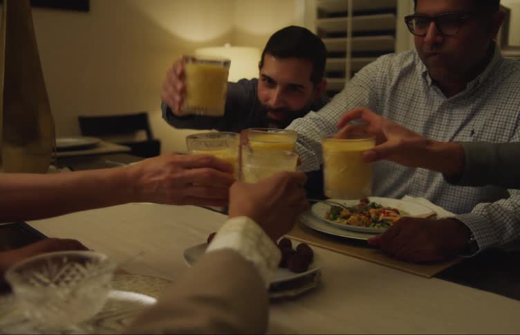 A group of people eating together in a home dining room table tap their glasses together in toast