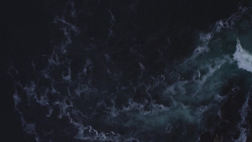 Ocean waves splashing and foaming against rocks in a dark sea