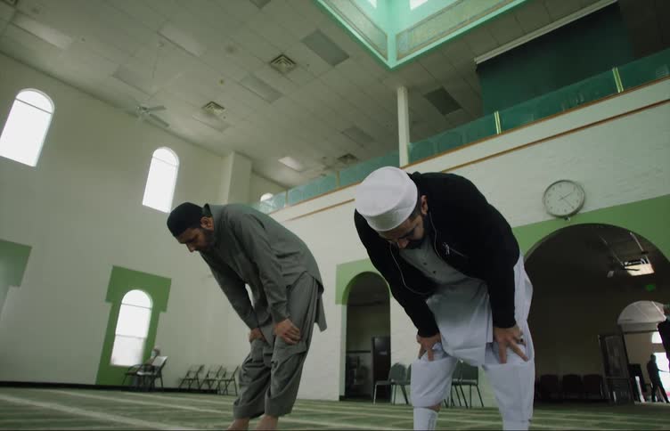 Two muslim men lean forward while praying in a mosque