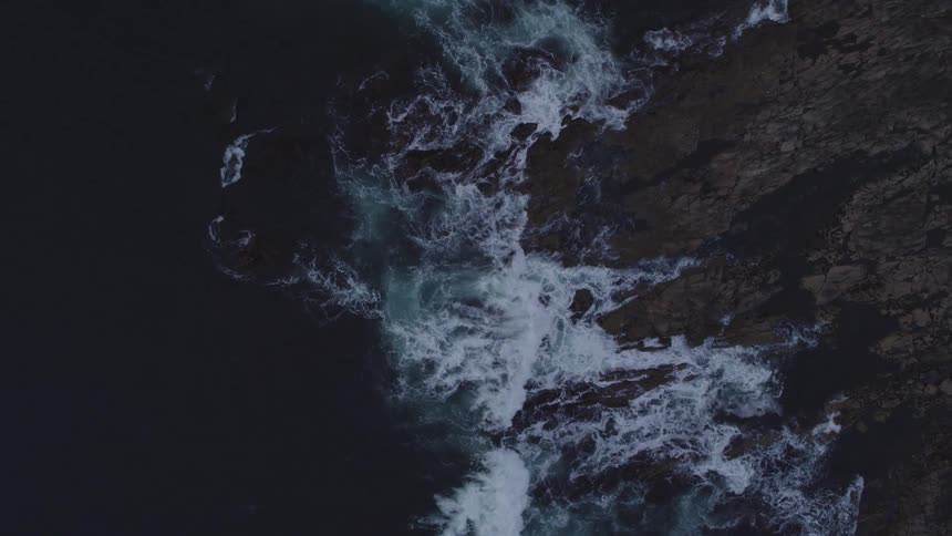 Aerial view of ocean waves breaking against cliff