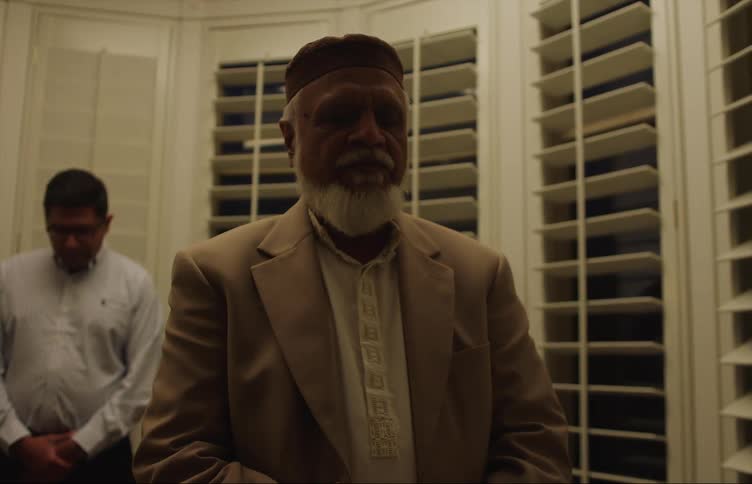 Two middle eastern muslim men standing near the window and praying with closed eyes at night