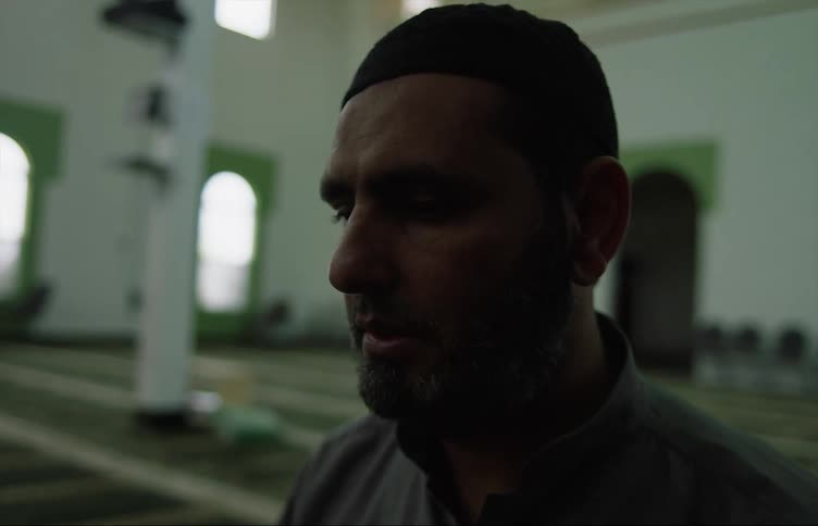 Man with beard and gray shirt prays at the mosque