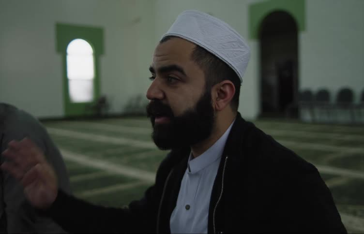 A man is sitting in a mosque talking with other men