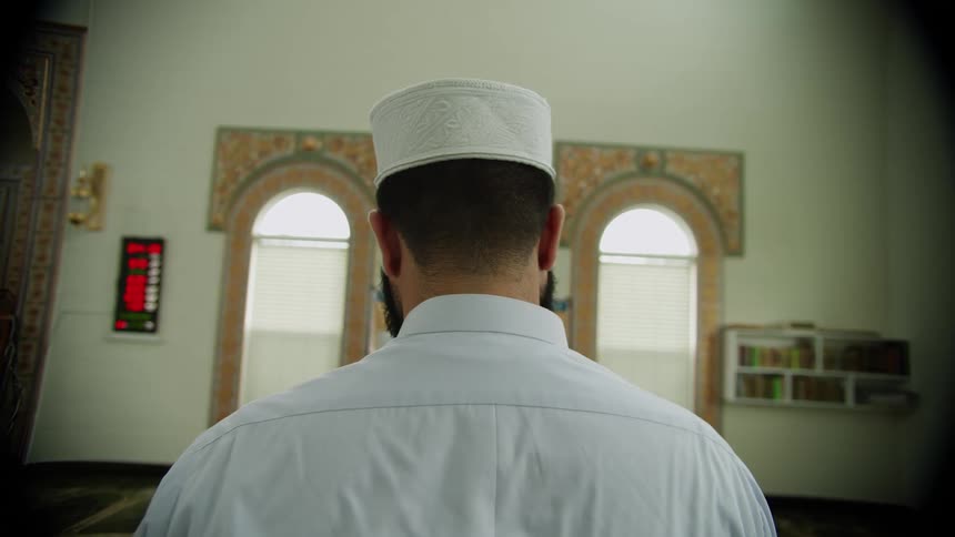 Man bows his head to the ornately carpeted floor while praying