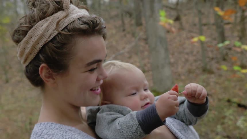 A woman holds a baby in the woods