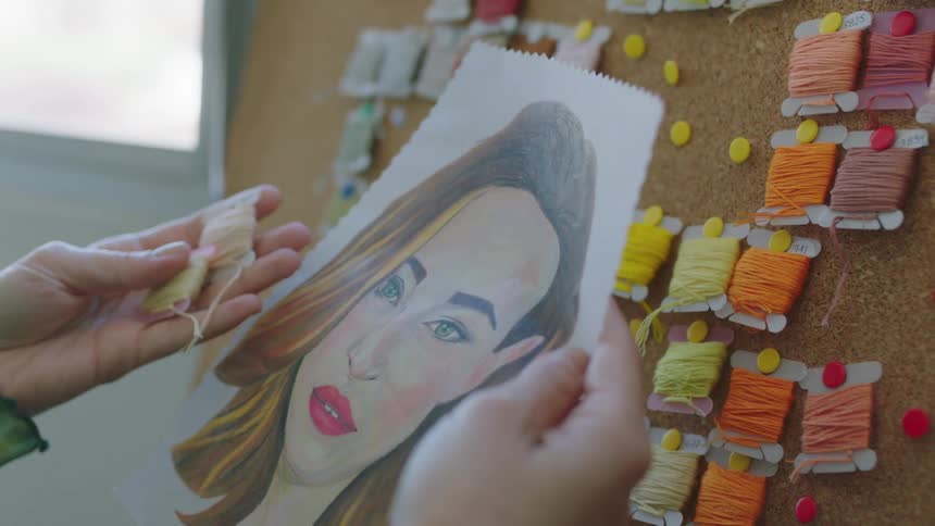A person references a color sketch while checking the colors of spools of thread