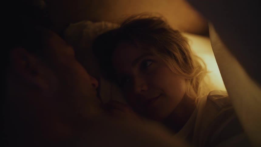 Happy young couple lying in the bed under the blanket romantically staring and caressing each other