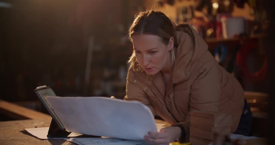 A woman looks through blueprints while also scrolling through a tablet