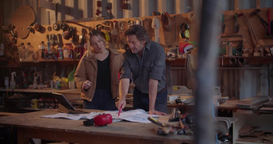 A man and woman standing at a table in a workshop discussing plans on paper