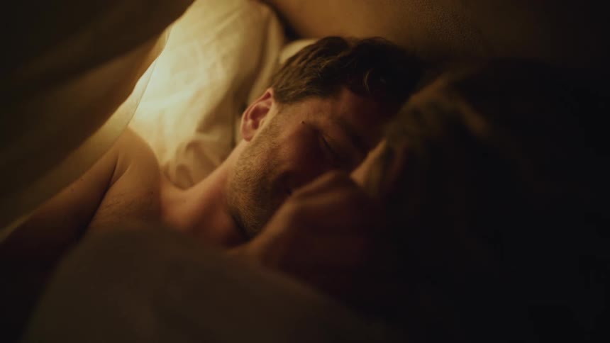 Happy young couple lying in the bed under the blanket facing one another cuddling and interacting in a romantic way