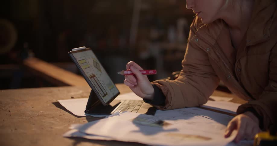 A woman scrolls through a tablet while looking over blueprints