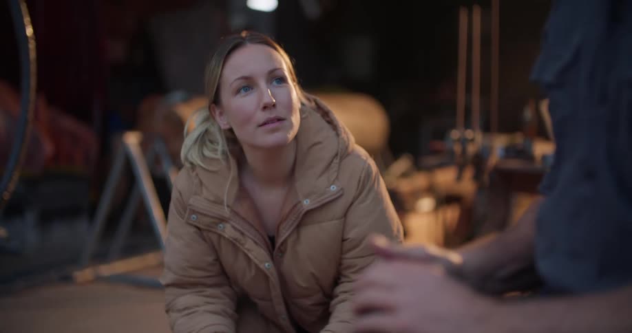 A woman is sitting inside a garage talking to a man