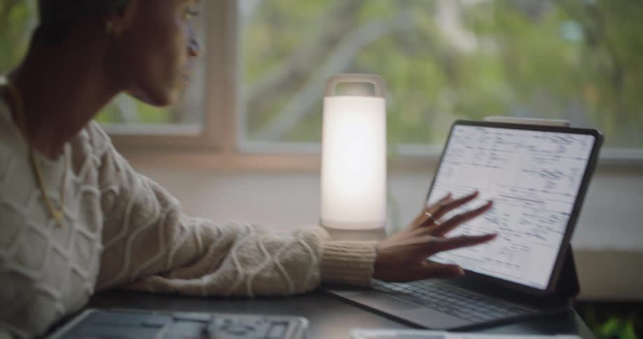 Woman sits at table working on open laptop computer while consulting system diagram on a touchscreen