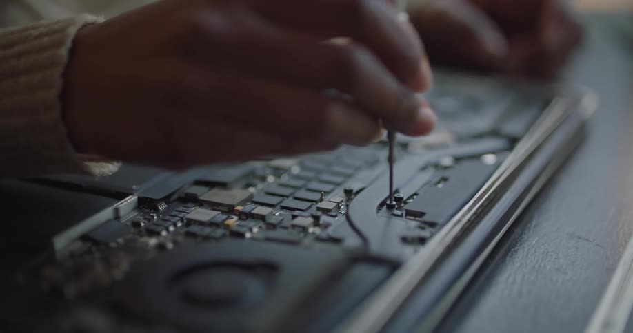A woman repairs uses a screwdriver as she repairs a laptop